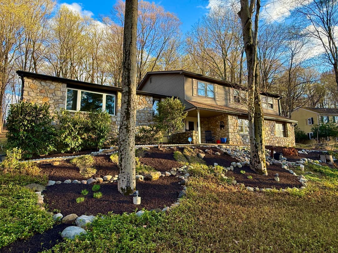 Beautiful stone house surrounded by lush greenery and landscaped yard in natural light.