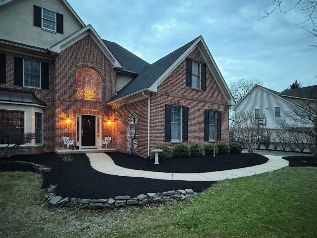 Elegant brick house with manicured landscaping and a curved walkway under evening sky.