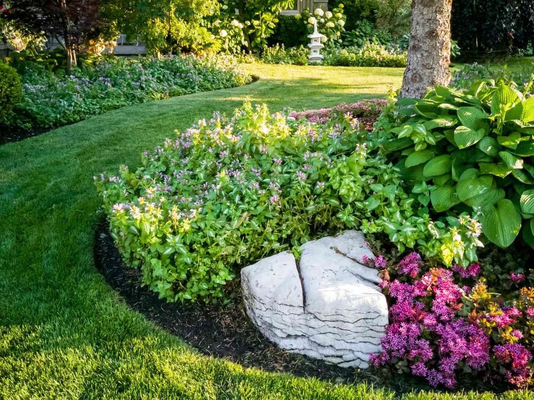 Lush garden with vibrant flowers, greenery, and a decorative stone in a curved landscape.