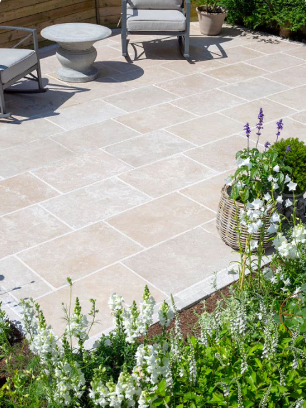 Patio with natural stone tiles, garden flowers, and outdoor seating in a lush setting.