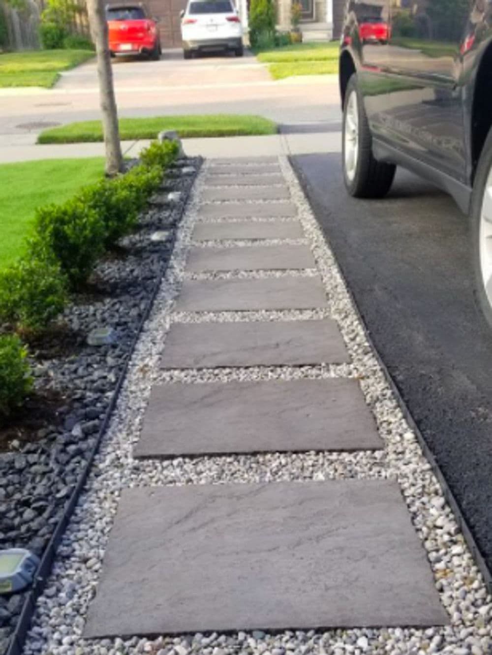 Decorative stone pathway with concrete slabs alongside a driveway and well-maintained shrubs.